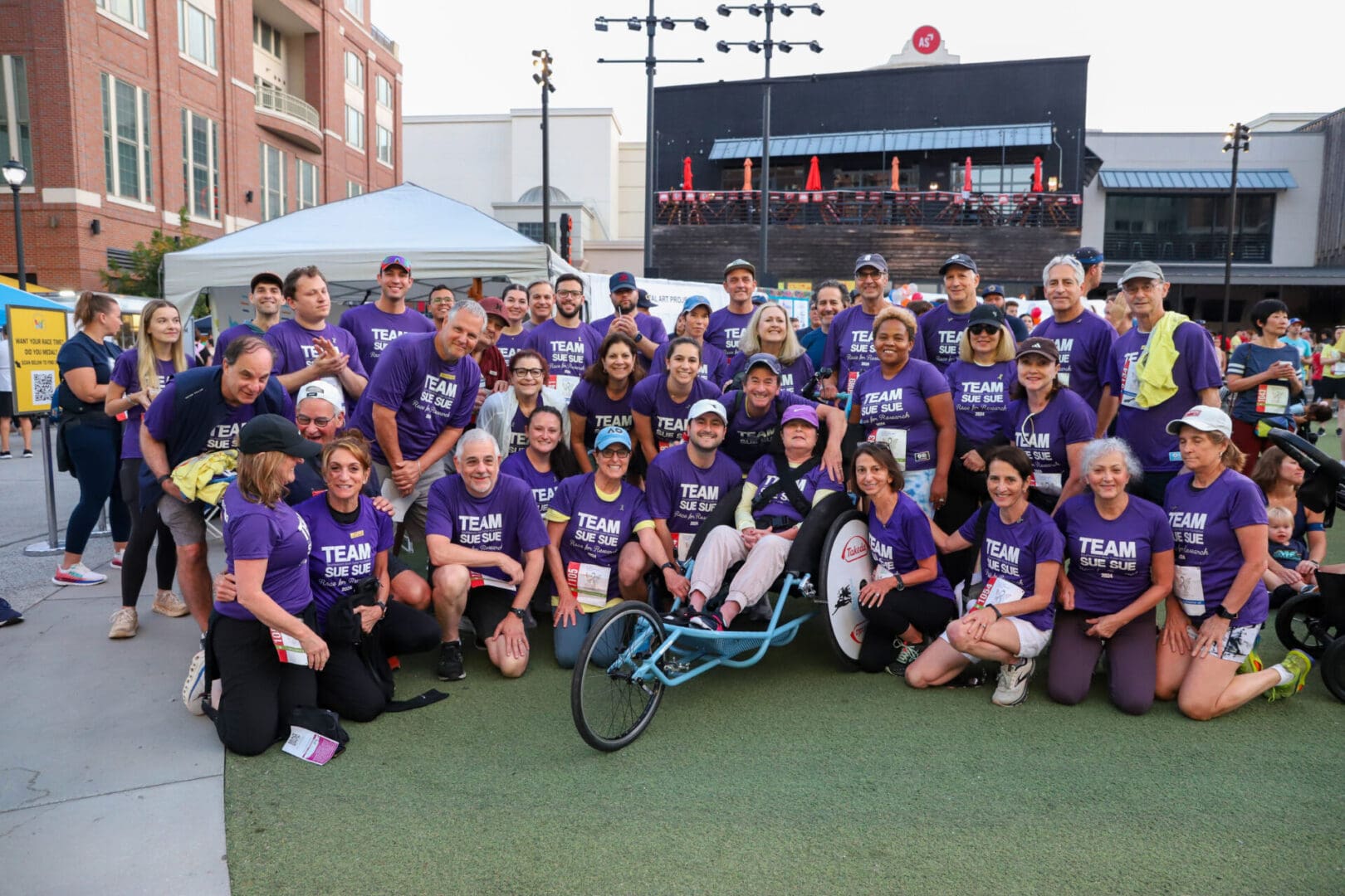 Group photo of people in purple shirts at an outdoor event.