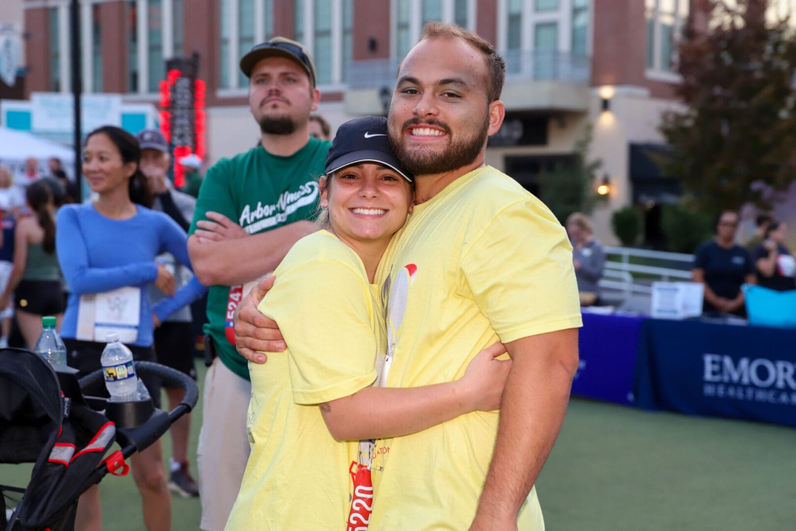 Two people in yellow shirts happily hugging outdoors at an event.
