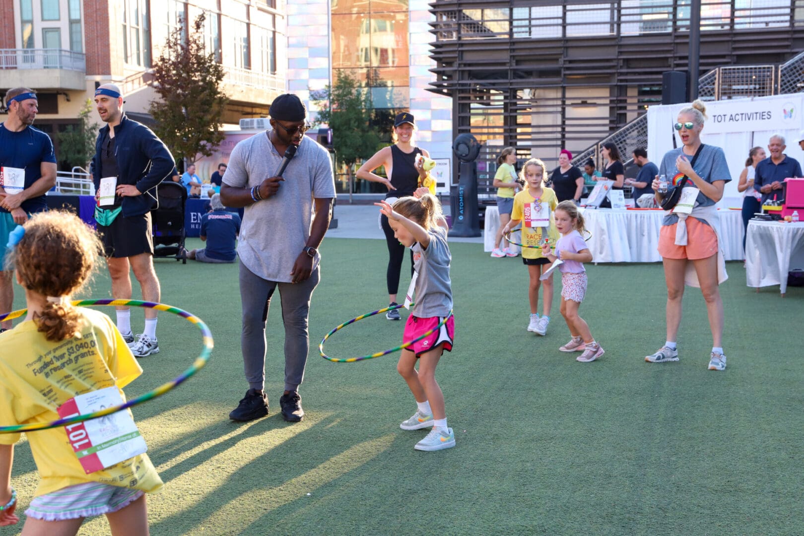 Children and adults playing with hula hoops outdoors on a sunny day.