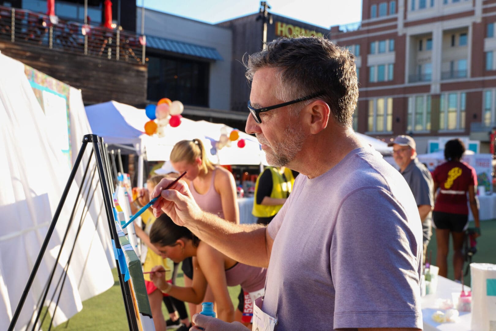 Man painting on a canvas outdoors at a fair or market.