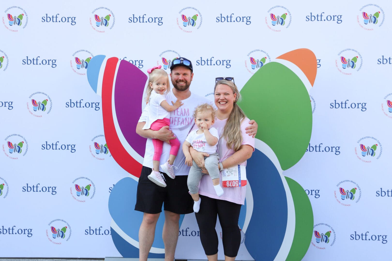A happy family of four posing outdoors with colorful butterfly wings behind them.