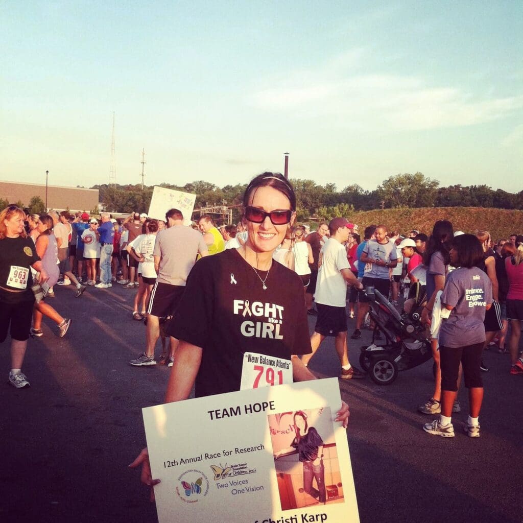 CiCi in a Fight Like a Girl shirt holding a Team Hope sign at a crowded race